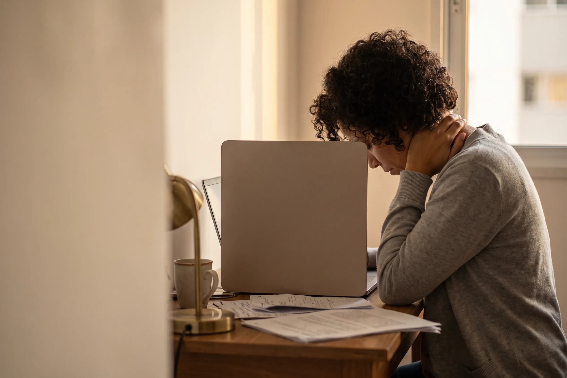 Adulto em frente ao computador levando a mão à nuca por dor no pescoço